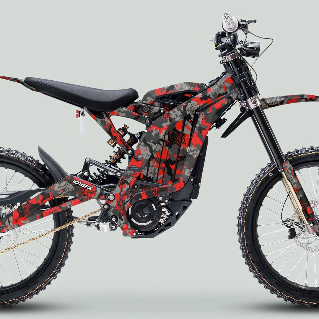 Side view of Surron Light Bee X Graphics Kit SPLAT CAMO Red on an off-road e-bike, showcasing rugged frame, suspension, and integrated motor for trail riding.