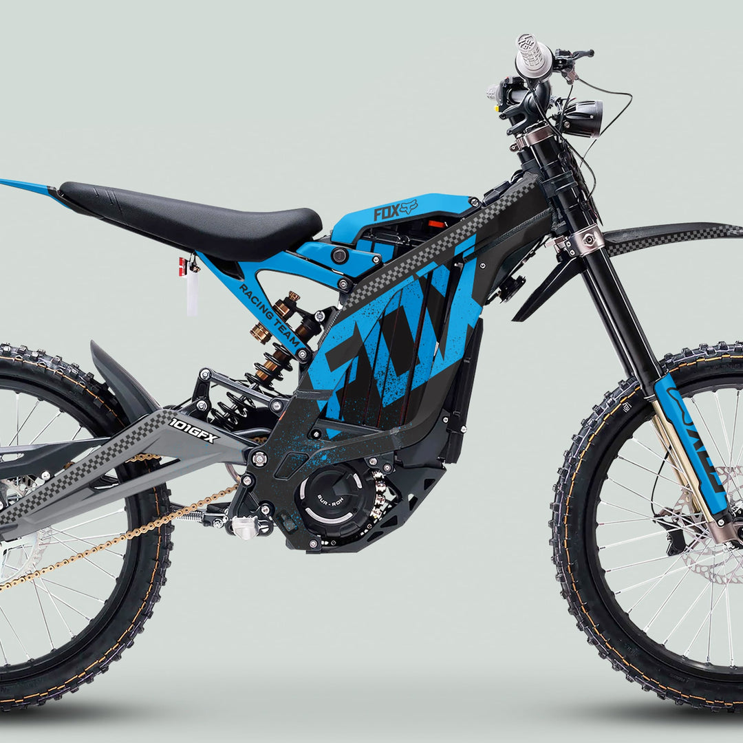 Side-view of Surron Light Bee X Graphics Kit FOX DUST Black Cyan on electric dirt bike, showcasing blue tubular frame, knobby tires, and motocross seat.