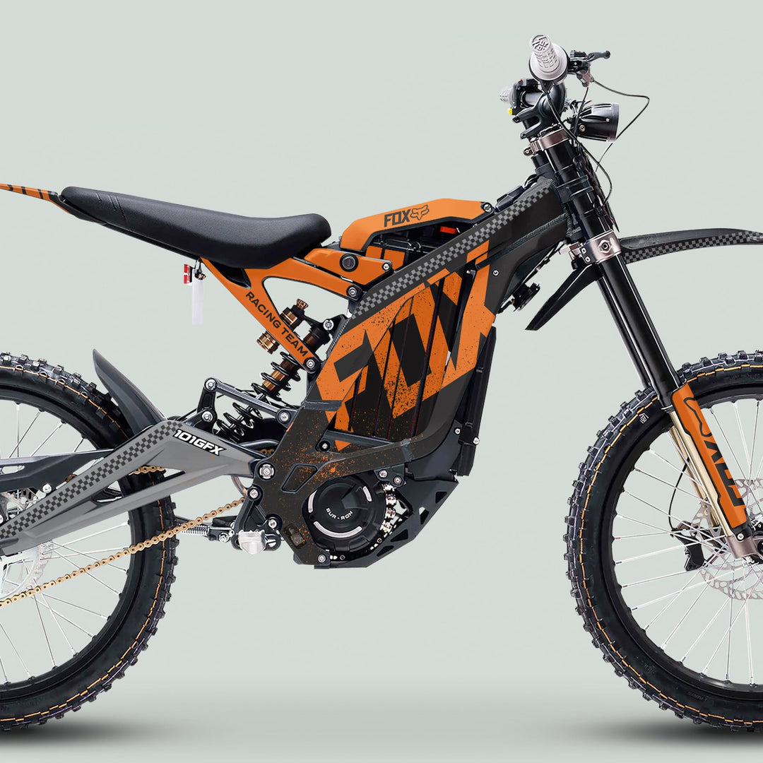 Surron Light Bee X Graphics Kit FOX DUST Black Orange displayed on an e-dirtbike with tubular frame, bold decals, knobby tires, and long-travel suspension.