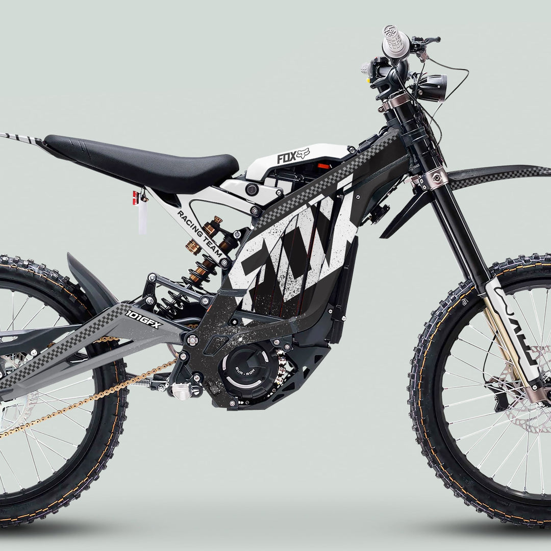 Side-profile of a Surron Light Bee X Graphics Kit FOX DUST Black White on an electric dirt bike, showcasing knobby tires, Fox shock, and central motor.
