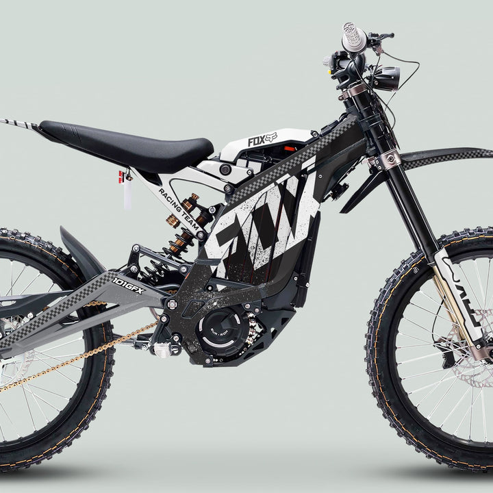 Side-profile of a Surron Light Bee X Graphics Kit FOX DUST Black White on an electric dirt bike, showcasing knobby tires, Fox shock, and central motor.