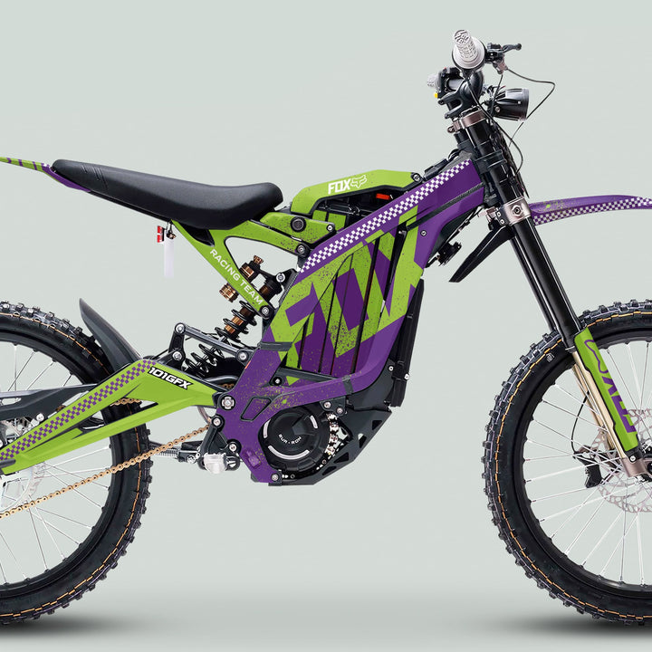 Side-profile of a Surron Light Bee X with FOX DUST Purple Green Graphics Kit, showcasing knobby tires, motocross-style seat, and battery housing.