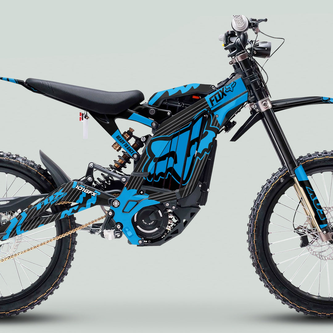 Side-view of an electric off-road motorcycle featuring the Surron Light Bee X Graphics Kit FOX STRIPES BLACK Cyan, highlighting knobby tires and Fox Racing graphics.