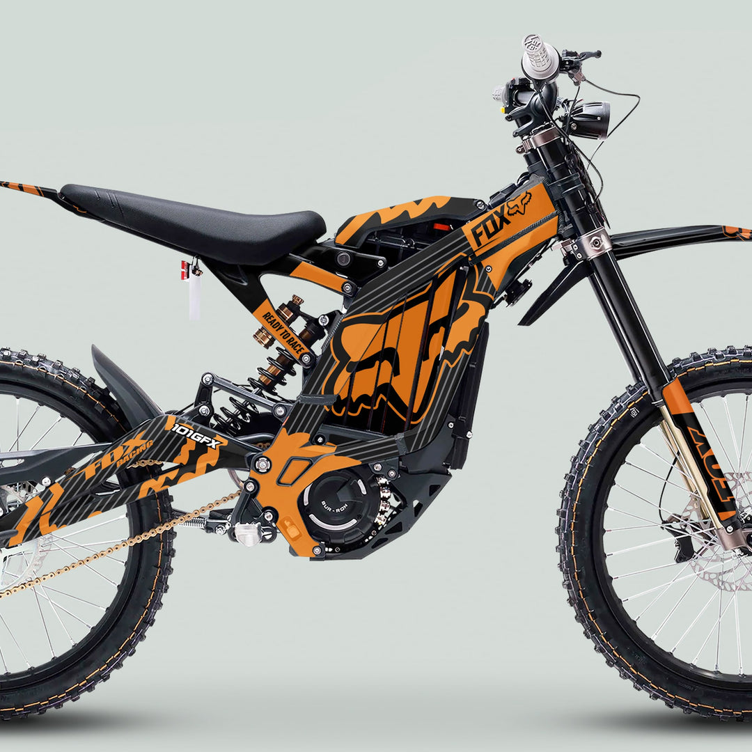 Surron Light Bee X Graphics Kit FOX STRIPES Black Orange on an off-road electric dirt bike with knobby tires, showcasing its sleek design and durable build.
