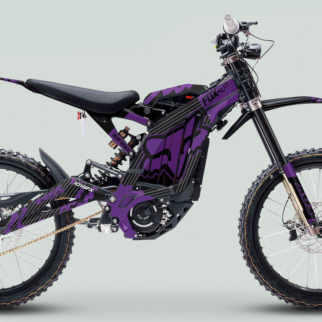 Side-on view of a Surron Light Bee X with FOX STRIPES BLACK Purple graphics kit, showcasing knobby tires, suspension forks, and distinctive fox-head logo design.