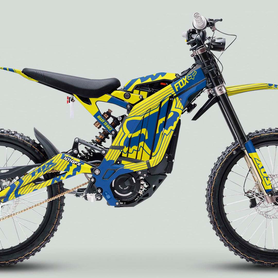Surron Light Bee X Graphics Kit FOX STRIPES YELLOW Blue on an electric dirt bike with knobby tires, long-travel suspension, and motocross-style seat.