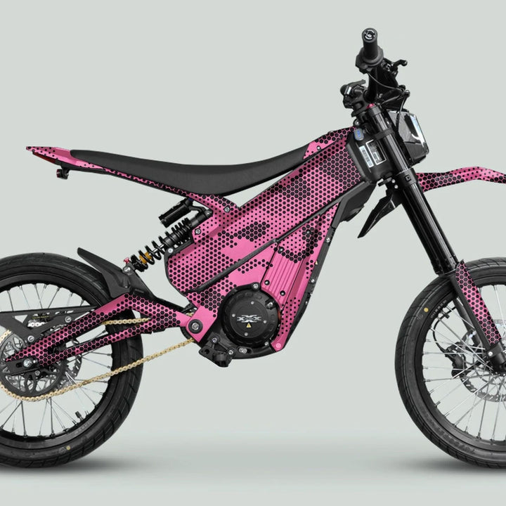 Side view of an electric motorcycle with Talaria XXX Graphics Kit HEXOCAM Pink, featuring a honeycomb-dot wrap and visible battery, shock absorber, and spoked wheels.